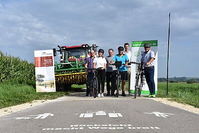 Gruppenbild Rücksicht macht Wege breit Der Bayerische Bauernverband, Dittenheimer Bürgermeister Ströbel, Landrat Manuel Westphal und Verena Ortner stehen am Radweg vor der Bodenaufschrift Rücksicht macht Wege breit. Ein Bulldog steht hinter der Gruppe und zwei Fahrräder stehen daneben.